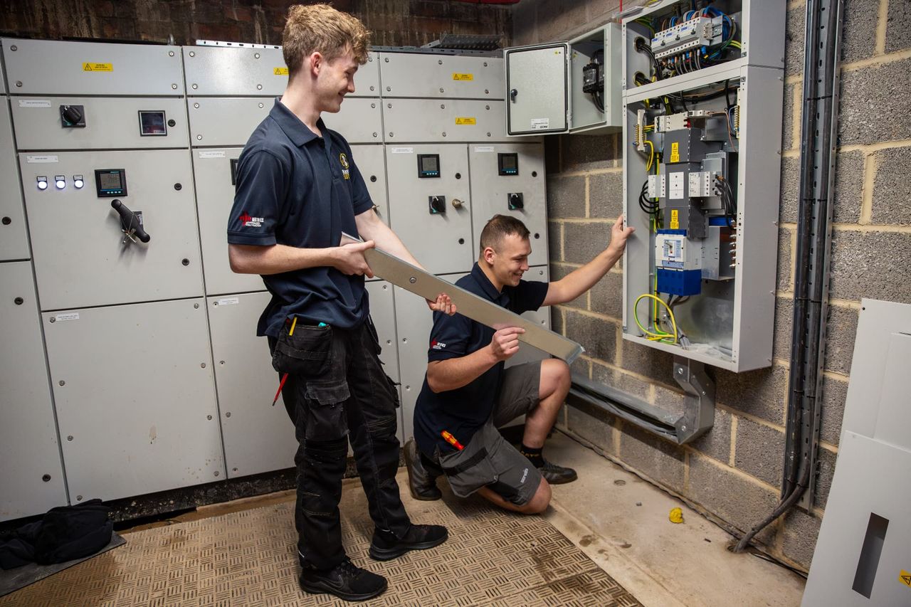 Two electricians checking plans beside a switchboard